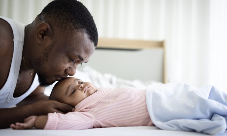 Black father kissing forehead of newborn daughter